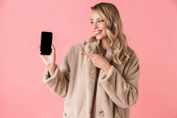 Hermosa mujer bonita joven feliz posando aislado sobre fondo de pared rosa que muestra la pantalla del teléfono móvil . — Foto de Stock