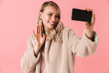 Genç güzel kadın pembe duvar arka plan üzerinde izole poz almak bir selfie cep telefonuyla.