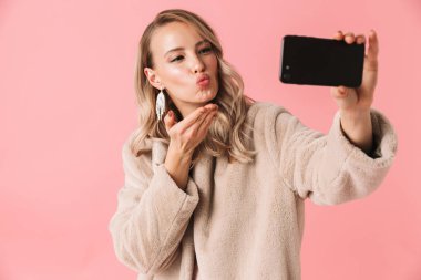 Genç güzel kadın pembe duvar arka plan üzerinde izole poz almak bir selfie cep telefonuyla.