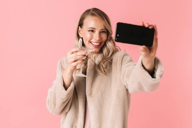 Genç güzel kadın pembe duvar arka plan üzerinde izole poz almak bir selfie cep telefonuyla.