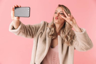 Genç güzel kadın pembe duvar arka plan üzerinde izole poz almak bir selfie cep telefonuyla.