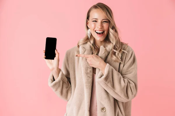 Hermosa mujer bonita joven feliz posando aislado sobre fondo de pared rosa que muestra la pantalla del teléfono móvil . — Foto de Stock