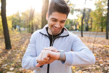Açık havada park izle saat bakarak kulaklık ile müzik dinleme içinde yakışıklı mutlu genç sporcu.