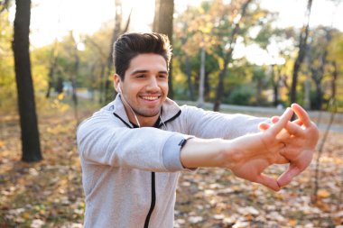 Yakışıklı genç sporcu açık havada park kulaklık ile müzik yapmak egzersizleri.