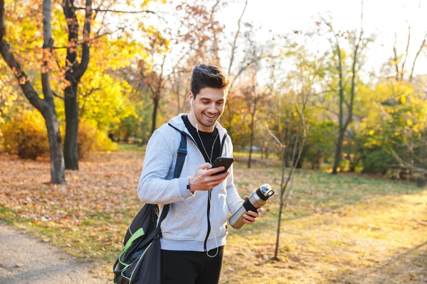 Αθλητής σε εξωτερικούς χώρους σε πάρκο ακούτε μουσική με ακουστικά χρησιμοποιώντας το κινητό τηλέφωνο. — Φωτογραφία Αρχείου