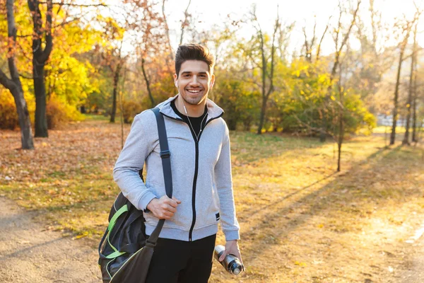 Αθλητής σε εξωτερικούς χώρους σε πάρκο ακούτε μουσική με ακουστικά, περπάτημα με τσάντα. — Φωτογραφία Αρχείου
