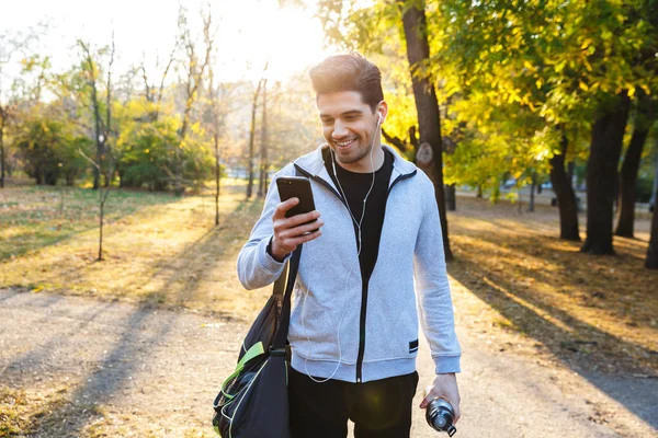 Sportsman venku v parku poslechu hudby pomocí sluchátek pomocí mobilního telefonu. — Stock fotografie