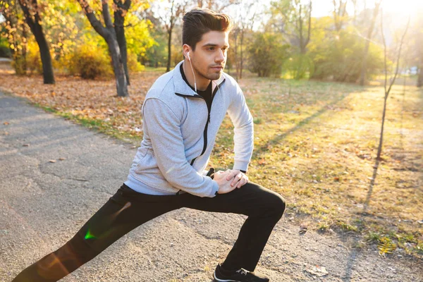 Bonito jovem desportista ao ar livre no parque ouvindo música com fones de ouvido fazer exercícios . — Fotografia de Stock