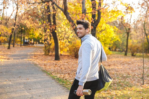 Deportista al aire libre en el parque escuchando música con auriculares caminando con bolsa . — Foto de Stock
