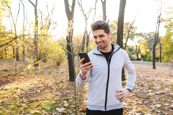 Jovem desportista feliz ao ar livre no parque ouvindo música com fones de ouvido usando telefone celular . — Fotografia de Stock