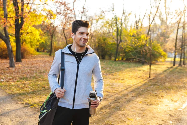 Αθλητής σε εξωτερικούς χώρους σε πάρκο ακούτε μουσική με ακουστικά, περπάτημα με τσάντα. — Φωτογραφία Αρχείου
