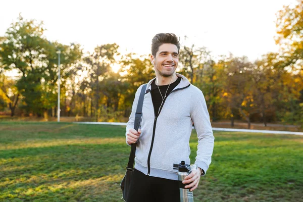 Sportler im Freien im Park Musik hören mit Kopfhörern gehen mit Tasche. — Stockfoto