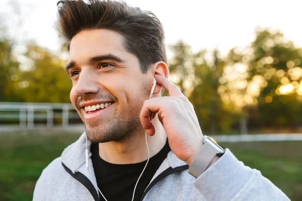 愉快的年轻运动员在户外公园听音乐用耳机. — 图库照片