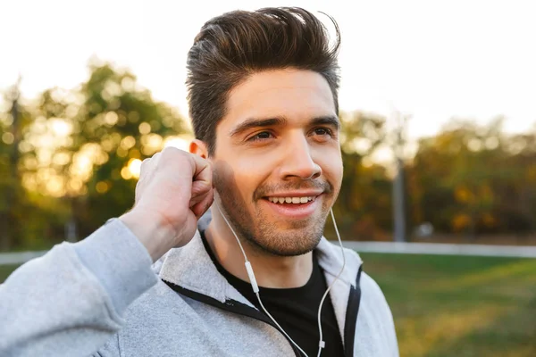 Gelukkig jonge sporter buiten in park luisteren muziek met koptelefoon. — Stockfoto