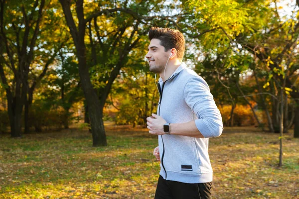 Junger Sportler im Park hört Musik mit laufenden Kopfhörern. — Stockfoto