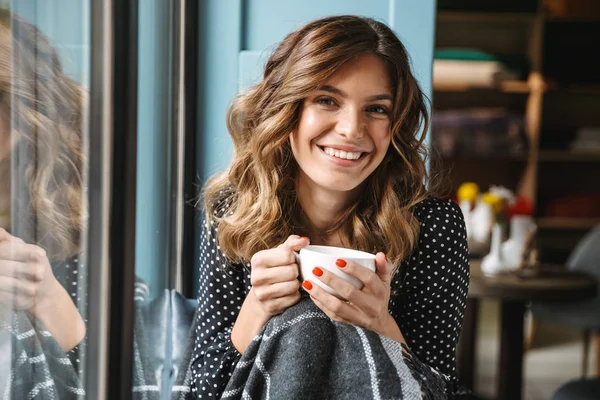 Smiling young woman sitting wrapped in blanket — Stock Photo, Image