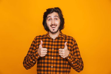 Başparmak gösterilen sarı duvar arka plan üzerinde izole mutlu yakışıklı genç.