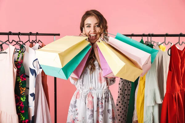 Фото счастливой девушки, стоящей в магазине возле вешалки с одеждой и держащей — стоковое фото