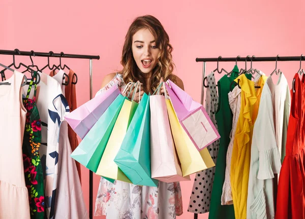 Foto de chica moderna de pie en la tienda cerca de perchero de ropa y alcohol —  Fotos de Stock