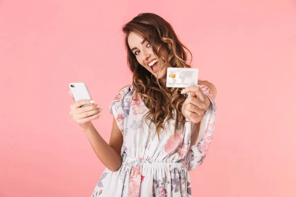 Foto de mulher positiva 20s em vestido segurando smartphone e crédito — Fotografia de Stock