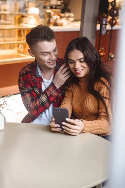 Молодая любящая пара сидит в кафе в помещении с помощью мобильного телефона . — стоковое фото