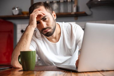 Sekmesini otururken gümüş dizüstü bilgisayar kullanan sinirli adam fotoğrafı