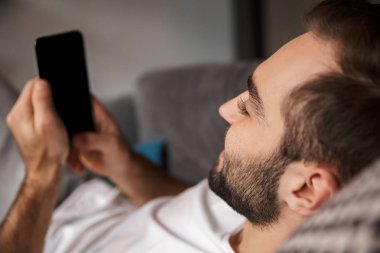 Sakallı adam tutarak ve yatan süre smartphone kullanarak fotoğraf