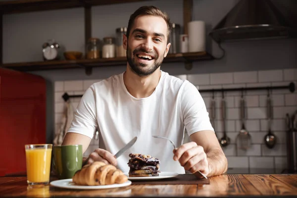 Portrait of positive man 30s eating while having breakfast in st