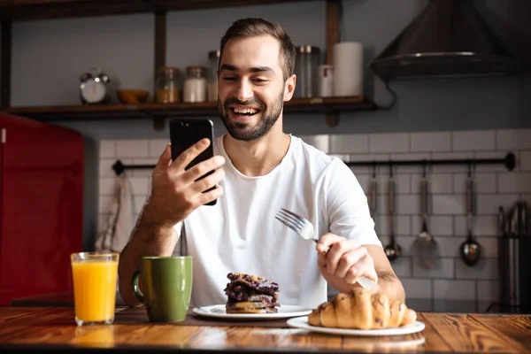 Portrait of young man 30s holding and using smartphone while hav — Stock Photo, Image