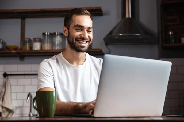 Photo of unshaved man using silver laptop while sitting at table