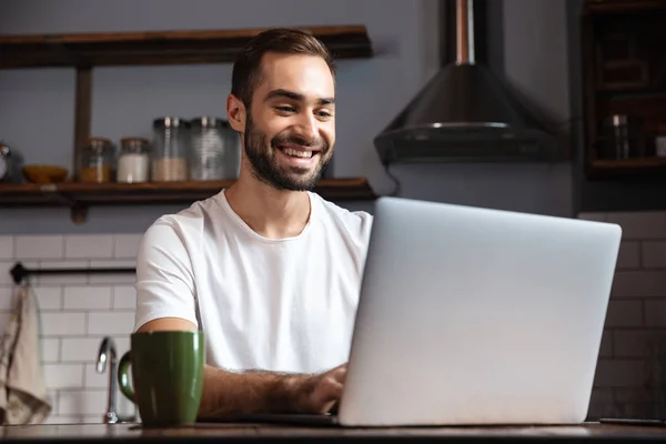 Foto eines unrasierten Mannes mit silbernem Laptop am Tisch — Stockfoto