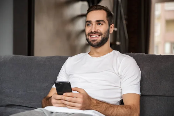 Foto de hombre caucásico sosteniendo y usando teléfono inteligente mientras está sentado — Foto de Stock