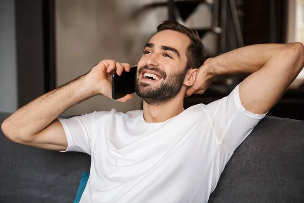 Фото радостного человека, разговаривающего на смартфоне, сидящего на диване — стоковое фото