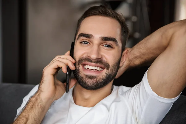 Foto von europäischem Mann, der auf Smartphone spricht, während er auf sof sitzt — Stockfoto