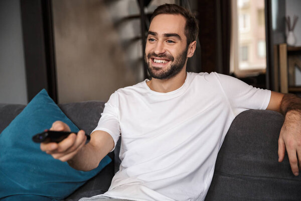 Photo of caucasian bachelor holding remote control while sitting