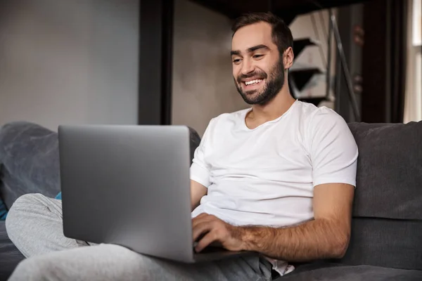 Photo of brunette bachelor using silver laptop while sitting on