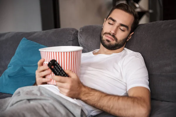 Foto de hombre caucásico sosteniendo palomitas de maíz cubo mientras duerme en —  Fotos de Stock