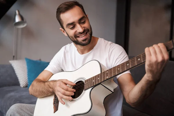 Foto de un hombre atractivo tocando la guitarra acústica mientras está sentado en — Foto de Stock
