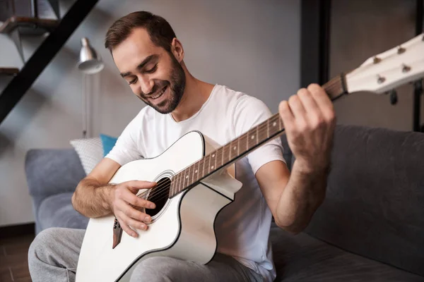 Foto de un hombre positivo tocando la guitarra acústica mientras está sentado en s — Foto de Stock