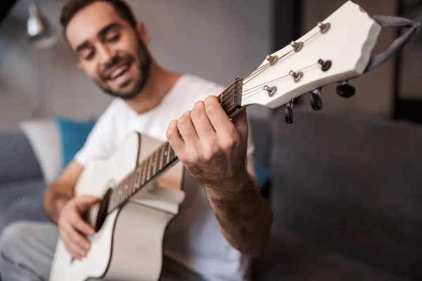 Foto de un hombre guapo tocando la guitarra acústica mientras está sentado en s — Foto de Stock