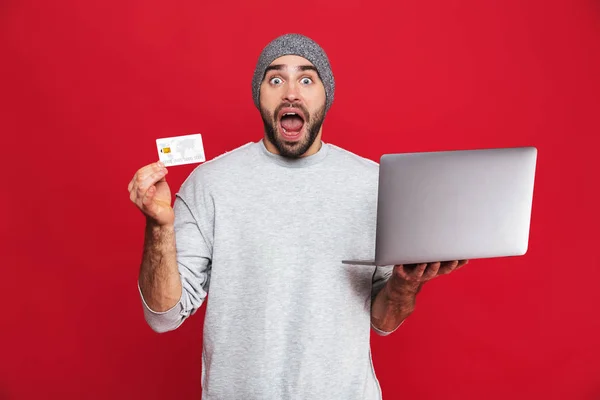 Foto de chico atractivo sosteniendo tarjeta de crédito y portátil de plata es — Foto de Stock