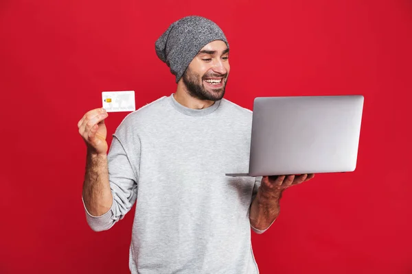 Фото невдалого хлопця, який тримає кредитну картку та ізольований срібний ноутбук — стокове фото