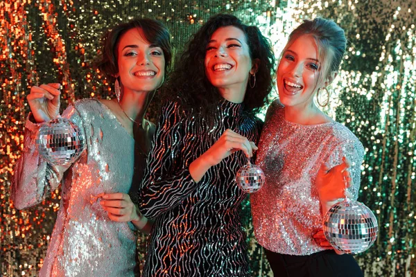Vrienden van de mooie jonge gelukkig vrouwen poseren op glitter muur achtergrond houden weinig mini speelgoed disco ballen. — Stockfoto