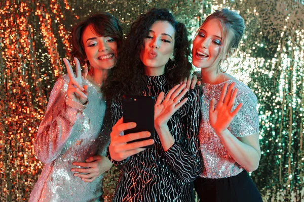 Vrienden van de mooie jonge gelukkig vrouwen poseren op glitter muur achtergrond nemen een selfie per telefoon. — Stockfoto