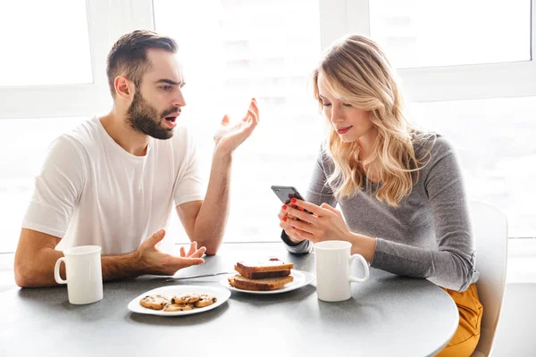 Pareja amorosa sentada en la cocina desayunar con teléfono móvil . — Foto de Stock