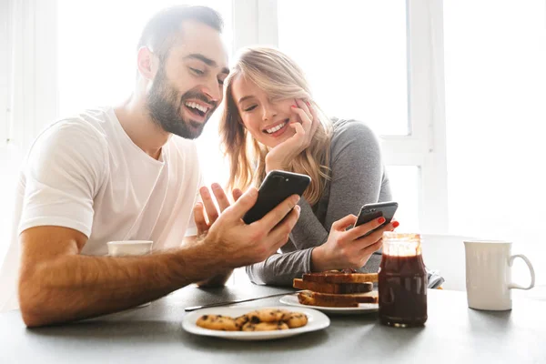 Milující pár sedící u kuchyně snídat používání mobilních telefonů. — Stock fotografie