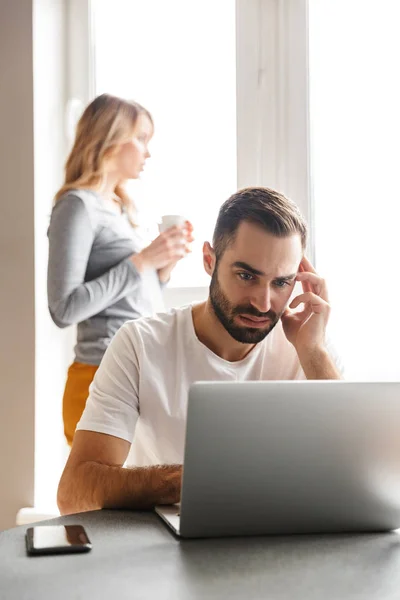 Pareja joven y cariñosa sentada en la cocina usando computadora portátil . —  Fotos de Stock