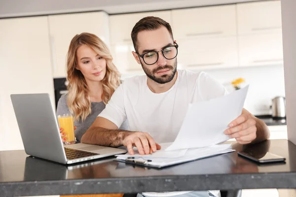 Pareja joven y cariñosa sentada en la cocina usando computadora portátil . — Foto de Stock