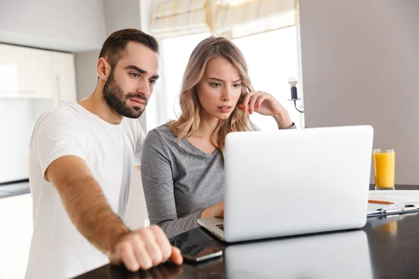 Pareja joven y cariñosa sentada en la cocina usando computadora portátil . —  Fotos de Stock