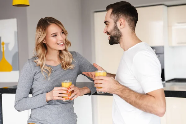 Joven pareja amorosa en la cocina bebiendo jugo hablando entre sí . — Foto de Stock